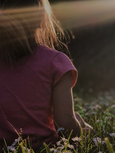 girl in pink shirt sitting in a field