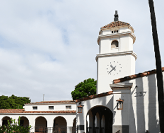A historic stone building with a clock tower and arches against a clear blue sky.